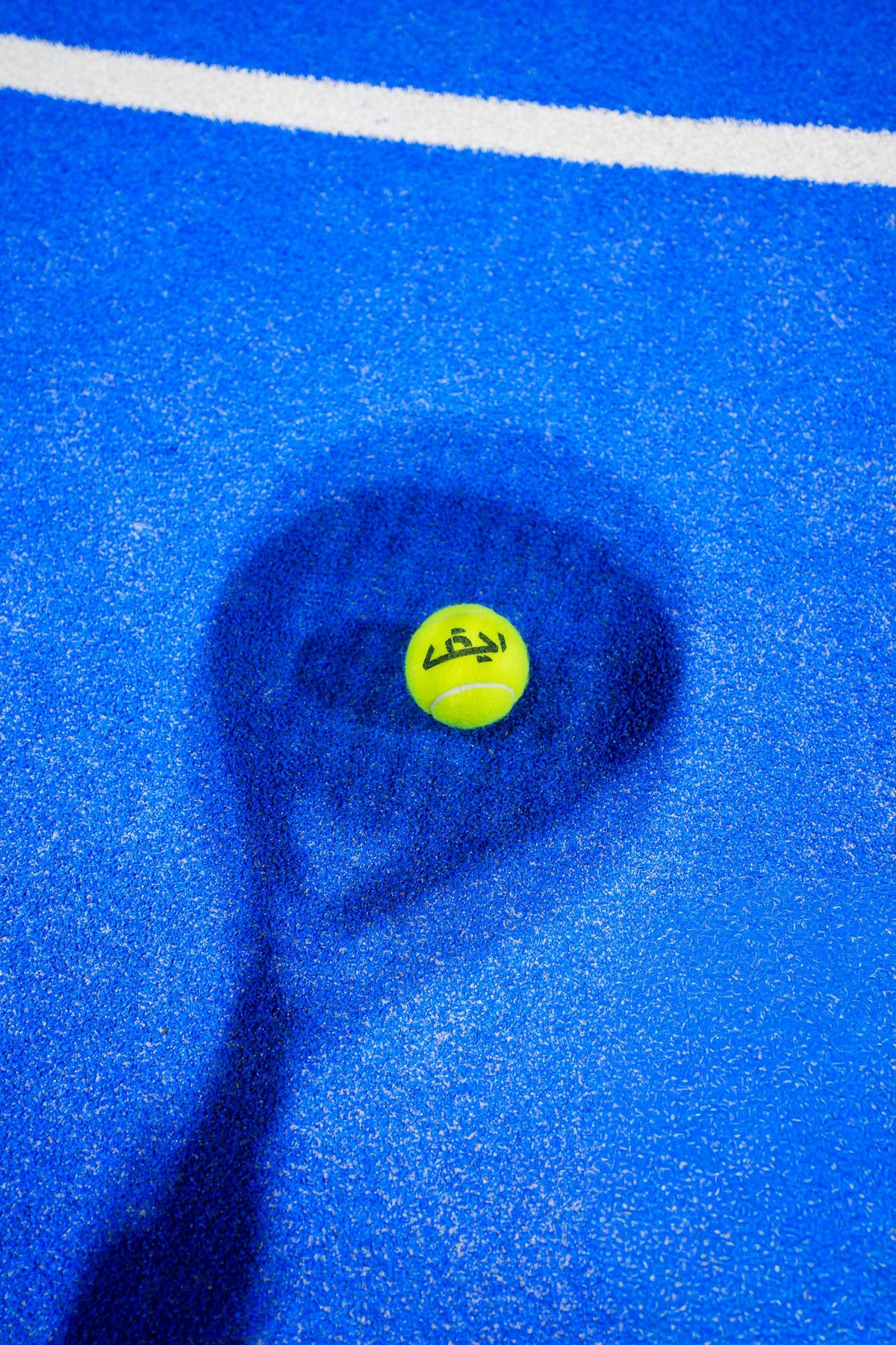 Padel ball and racket shadow on a blue padel court