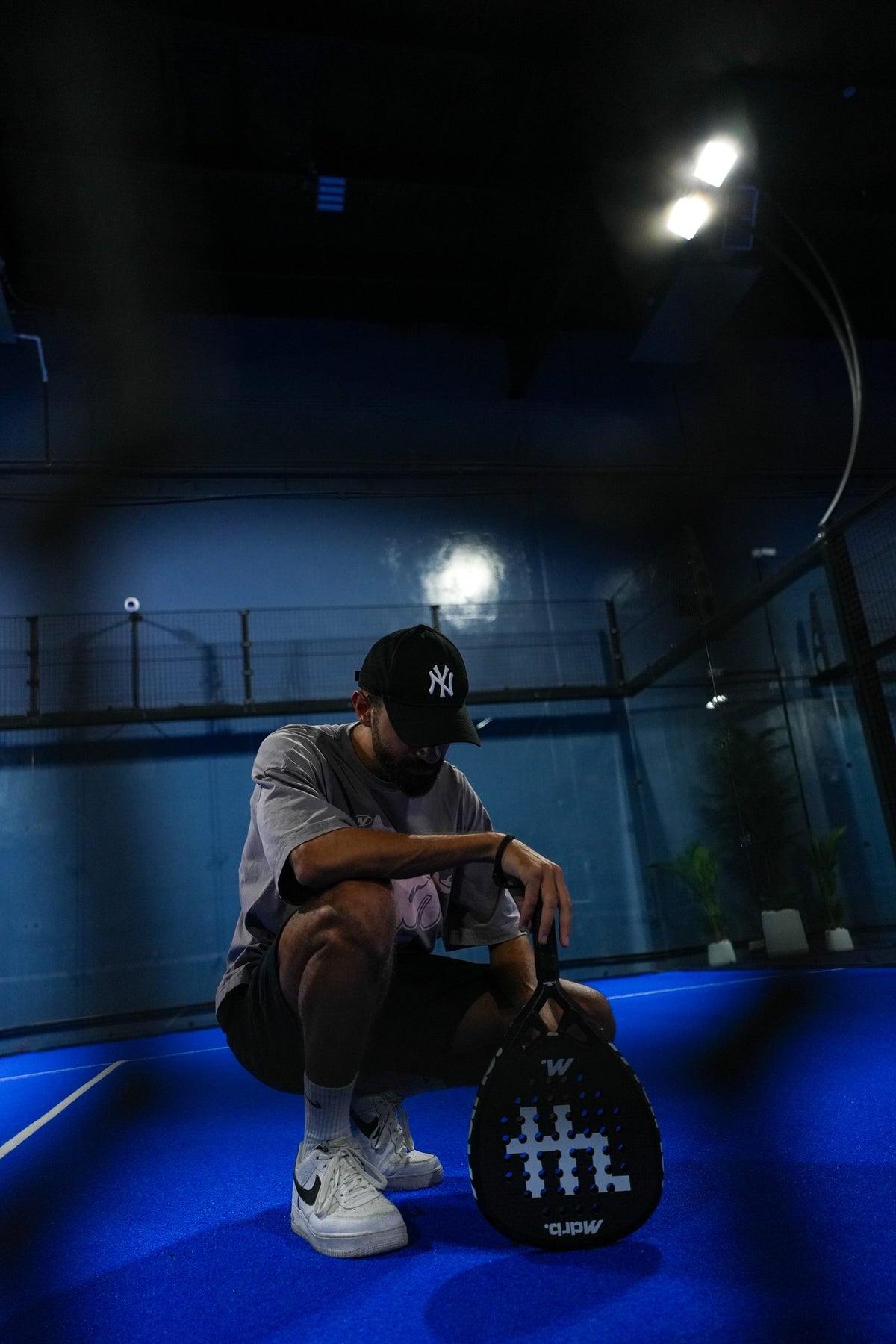 Player crouched on court with the MDRB Dark Matter padel racket